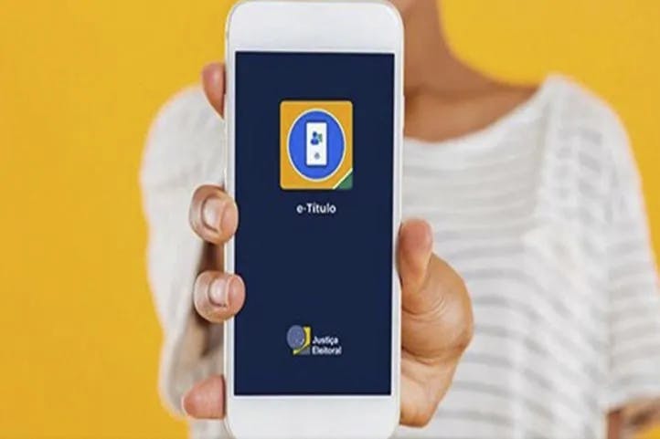 imagem colorida mostrando pessoa segurando celular e mostrando a tela com o aplicativo e-titulo