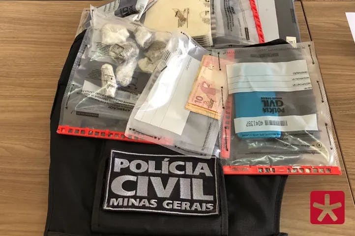  materiais apreendidos pela polícia em cima de uma mesa, armazenados em sacos plásticos contendo dinheiro, celular e drogas