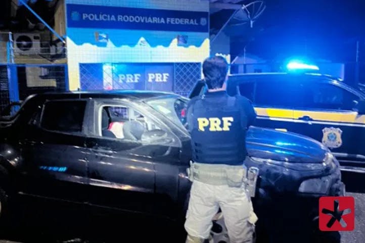 imagem colorida, contendo polícia rodoviária de costas e o veículo Fiat Toro de cor preta estacionado em frente ao posto policial da PRF