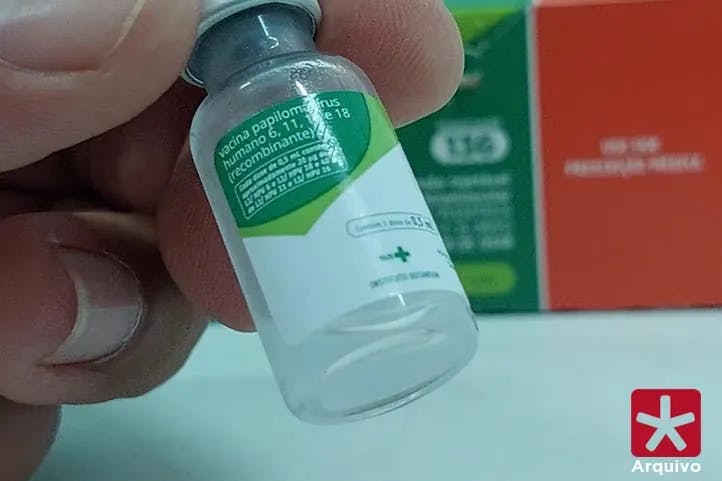 imagem colorida, mão segurando o frasco da vacina contra o HPV