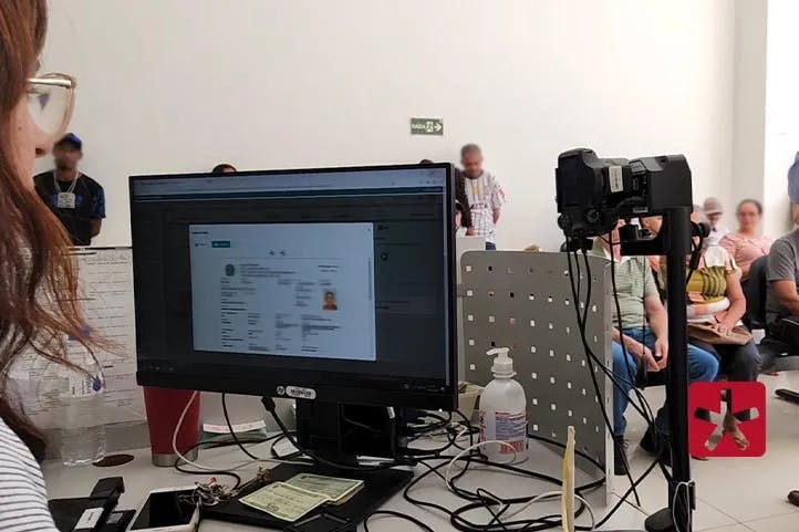 Imagem colorida mostrando atendimentos no cartório eleitoral em Patos de Minas com a tela do computador ao lado da atendente e pessoas sentadas na sala de espera.