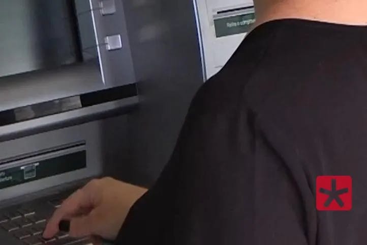 foto mostrando mulher em um caixa eletrônico dentro de agência bancária com a mão sobre o teclado.