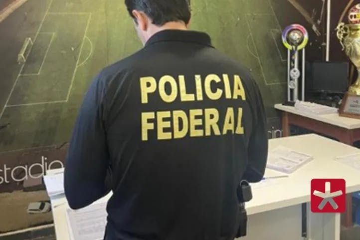 imagem colorida mostrando policial da PF de costas averiguando documentos