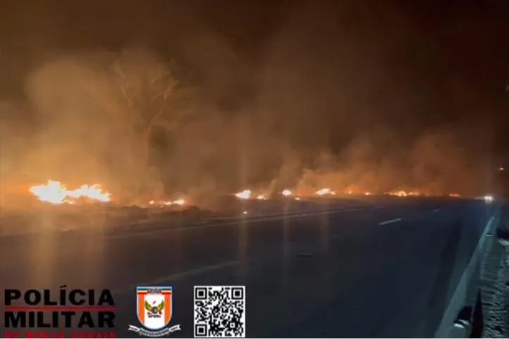 imagem colorida feita durante a noite, ,mostrando uma queimada na pastagem ao lado da rodovia provocando muita fumaça