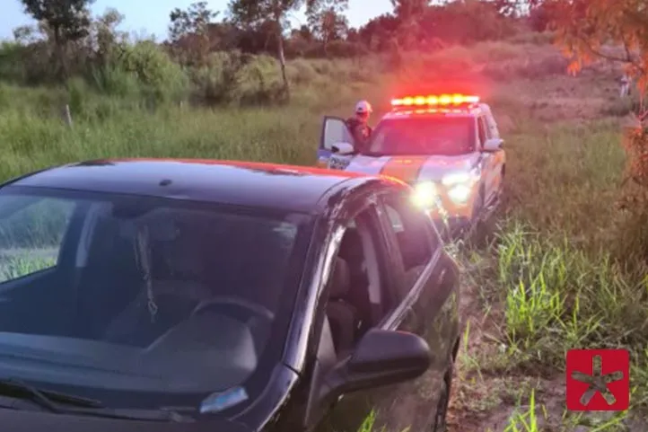 veículo Chevrolet Onix apreendido e logo atrás a viatura da PM com um militar ao lado