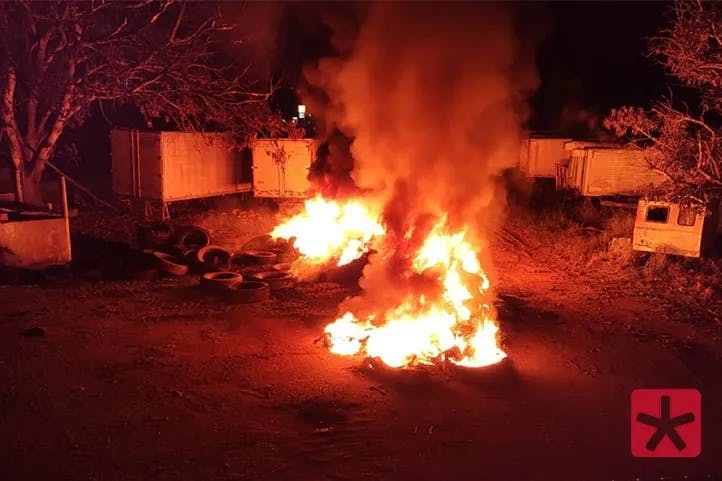 imagem colorida feita durante a noite, mostrando fogo com chamas altas nos pneus que estão no chão,