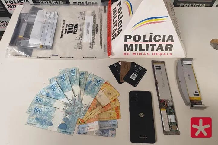 fotografica contendo prisma com logomarca da polícia militar e a frente dinheiro, celular , cartões de crédito e dispositivos eletrônicos